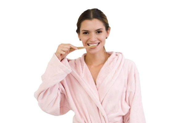 Woman with black hair in a pink shirt brushing her teeth to maintain good oral health