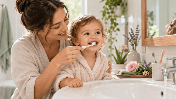Mother gently brushing her young child’s teeth with a soft toothbrush in a bright bathroom, representing children’s oral care, healthy brushing habits and early dental hygiene.
