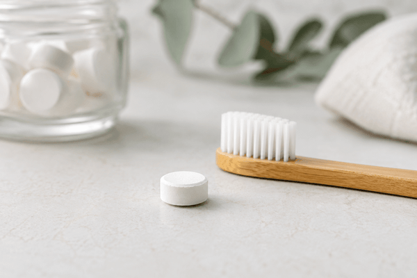Minimalist toothpaste tablets UK beside a bamboo toothbrush and glass jar, illustrating sustainable oral care in the UK.