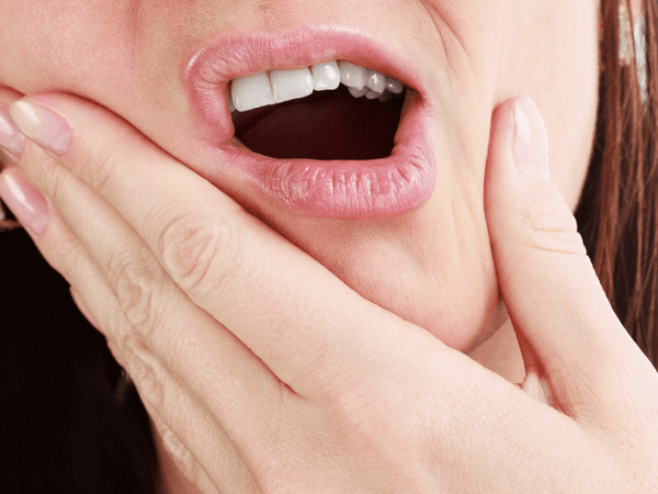 A close-up of a person holding their jaw in sudden pain after drinking cold liquids, illustrating temperature sensitivity.
