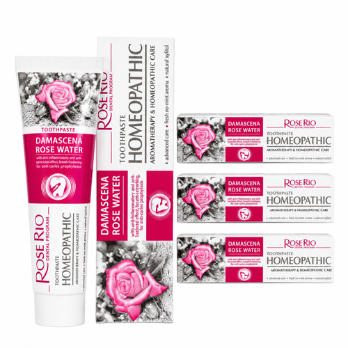 A 3-pack bundle of Rose Rio Homeopathic Toothpaste in Damascena Rose Water, featuring a tube and boxes on a reflective surface. The packaging denotes exact therapeutic claims: aromatherapy, anti-inflammatory, breath-refreshing, and anti-caries prophylaxis. Formulated with natural xylitol and a fresh no-mint aroma. Supplied by UK oral care retailer Edinco.