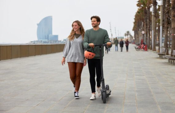 Couple walking alongside a Segway Ninebot MAX G30 Gen 2 scooter on a scenic boardwalk